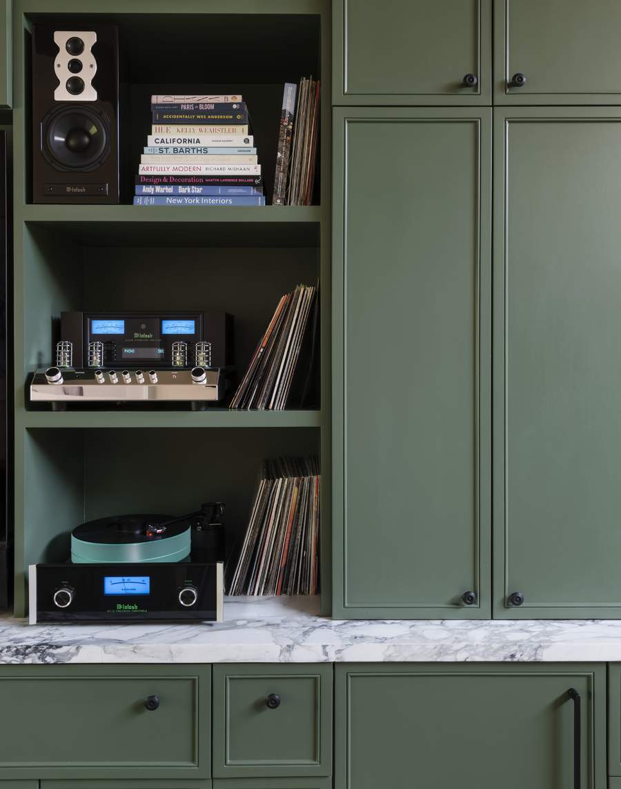 Close-up image of a fitted cabinet painted in a dark green color. There is a marble countertop and shelves that are open holding record players, speakers, and vinyl records.