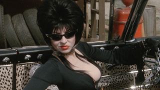 Elvira wearing sunglasses and low-cut dress behind the wheel of her car in Elvira: Mistress of the Dark