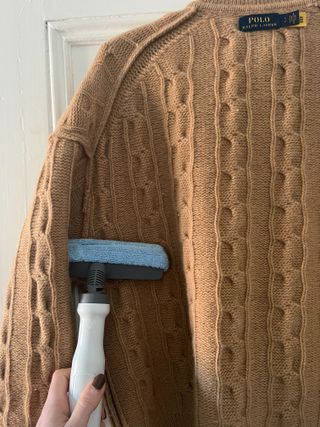 Using the fabric attachment to steam clean a brown jumper