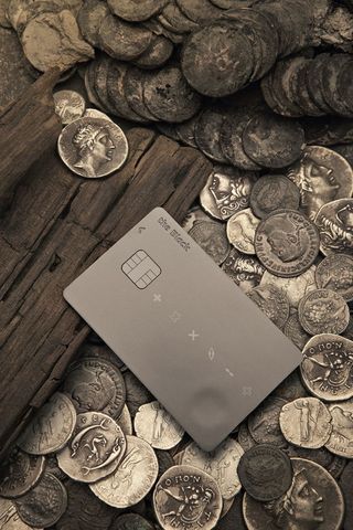 View of a black payment card pictured on top of multiple coins and a piece of wood
