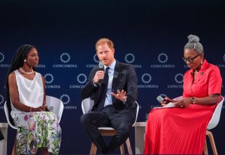 Prince Harry sitting on stage speaking into a mic with Tessy Ojo of The Diana Award and Christina Williams