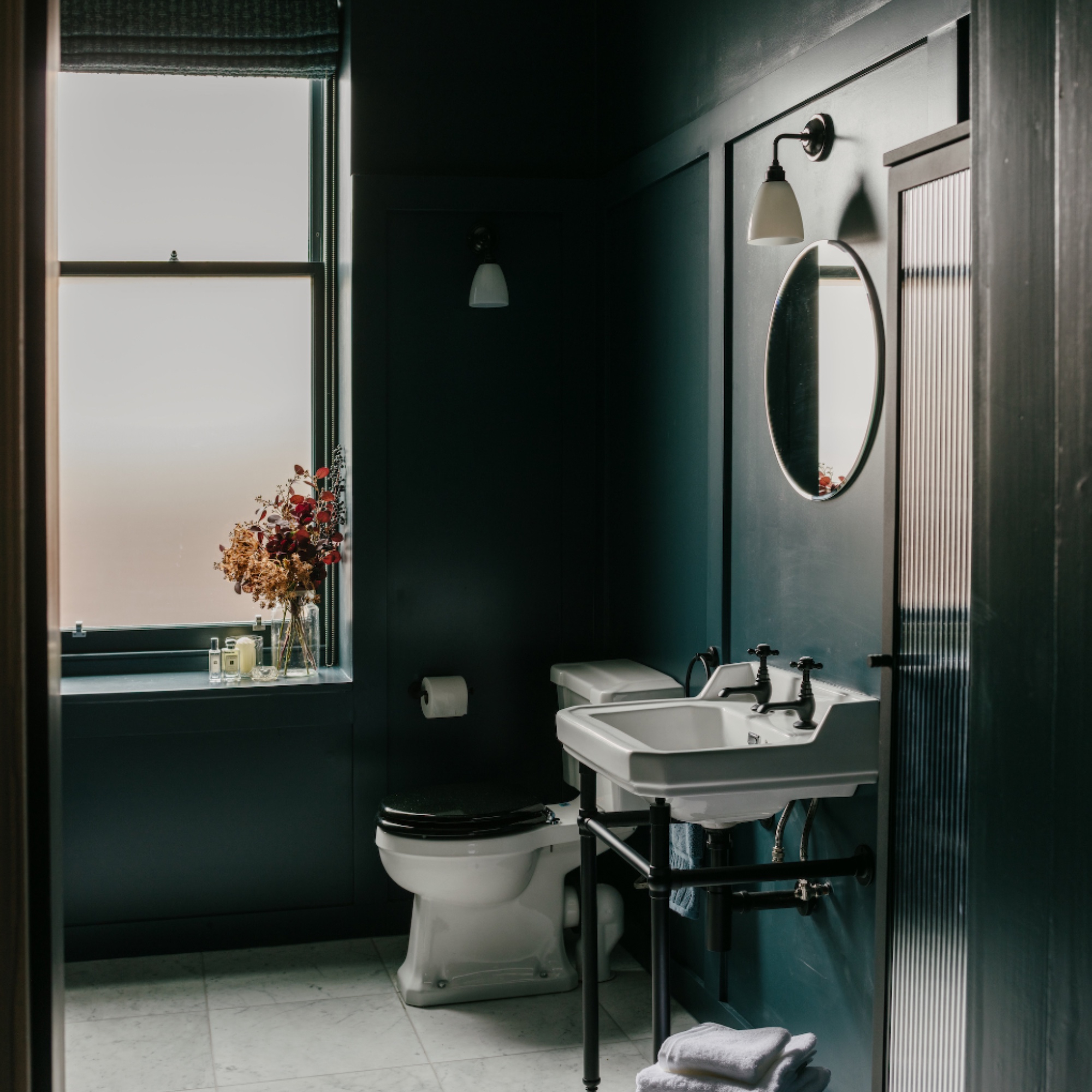 dark green bathroom with white sanitaryware, large window, wall lights