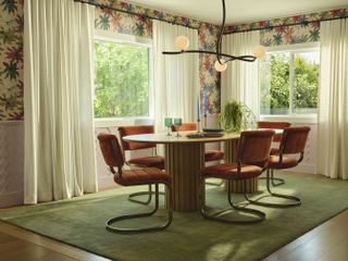 A dining room with a green carpet, oval dining table and floral wallpaper