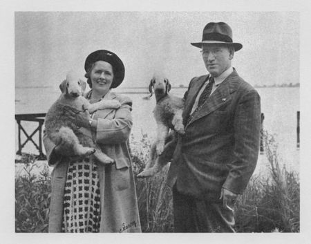 Anna and Anthony Neary stand outdoors, each holding a Bedlington Terrier &mdash; Ch. Rock Ridge Moving Belle and Ch. Rock Ridge Morning Dew.