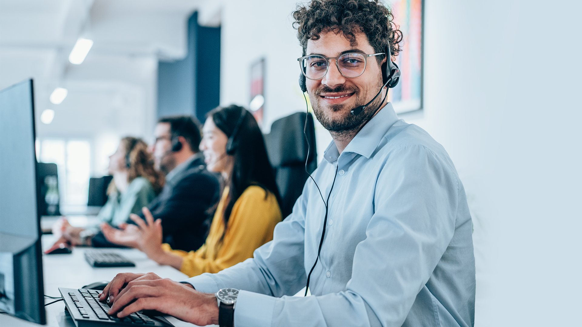 Portrait of call center operators working in the office. Call center agent working with his colleagues in modern office. Smiling handsome businessman working in call center.