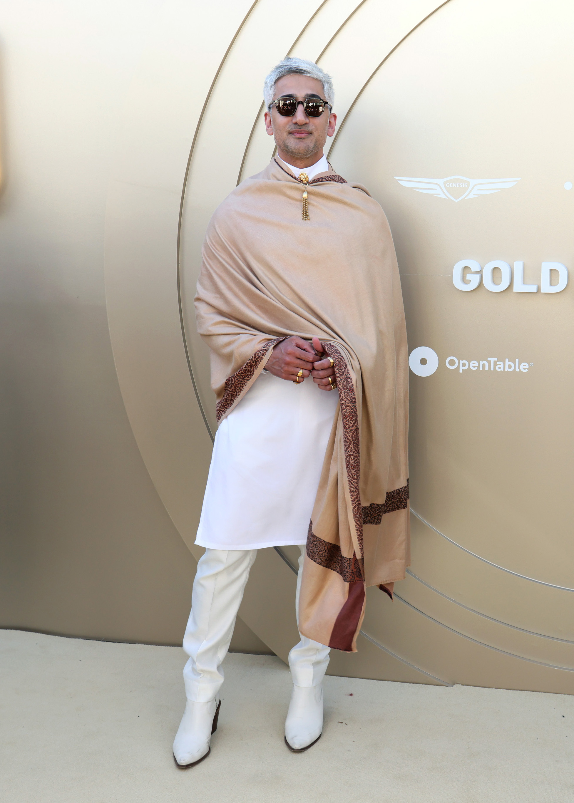 Tan France wearing a tan cape and a white tunic on a red carpet