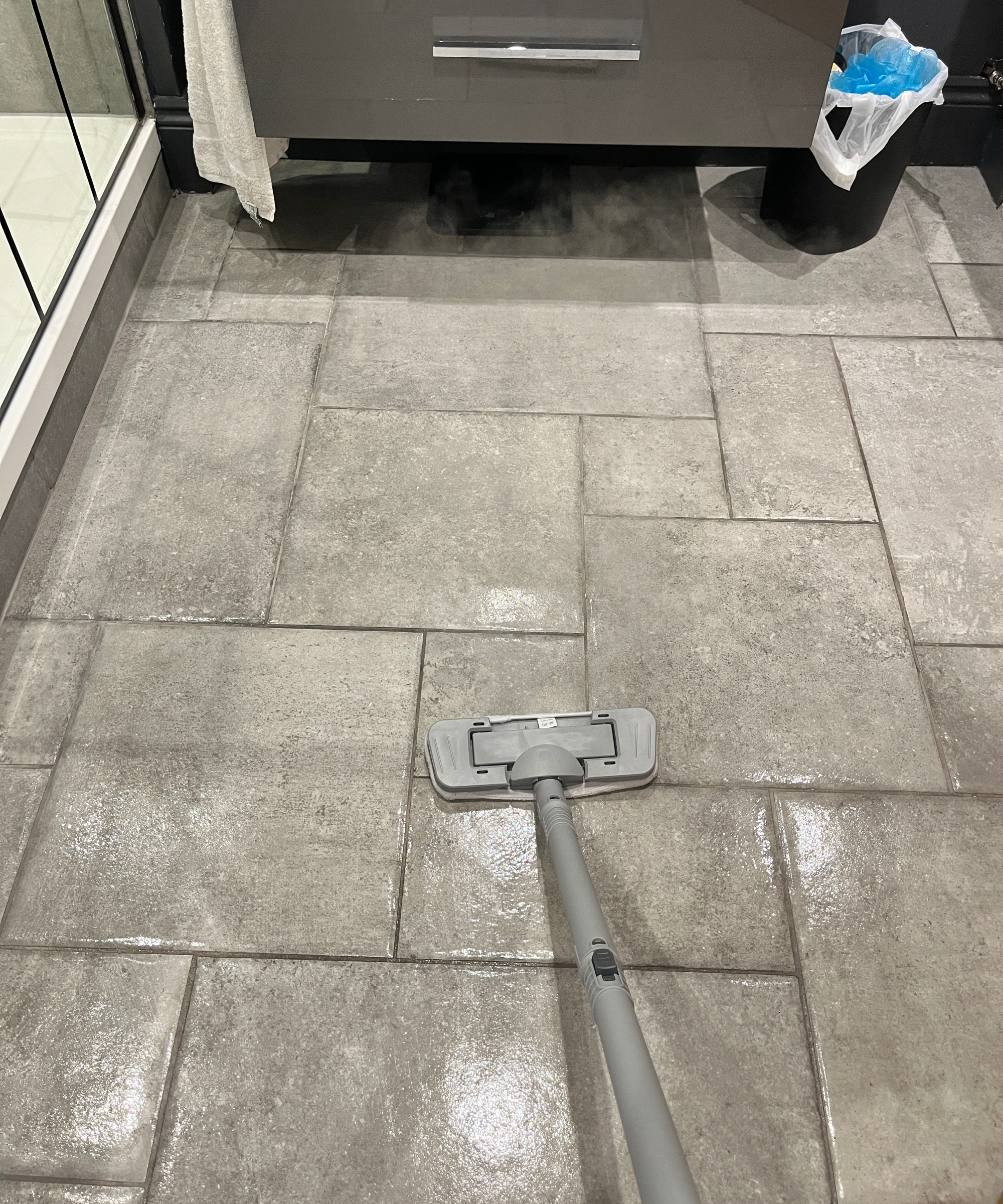 steam cleaner being used to mop grey tiled bathroom floor