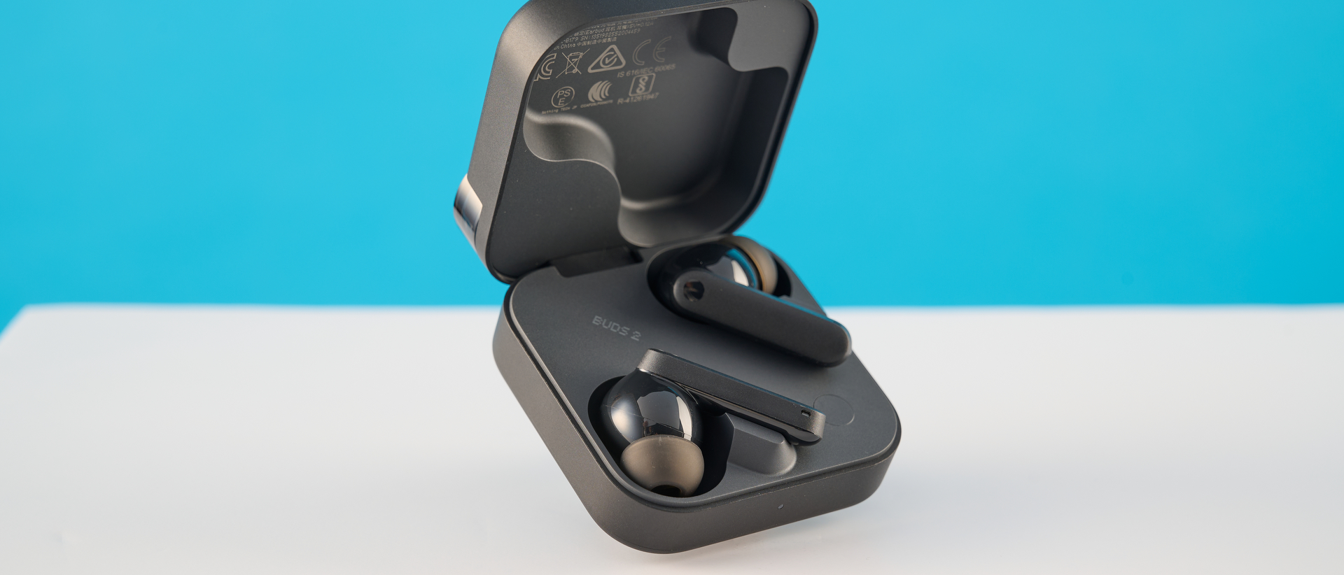 CMF Buds 2 in Dark Gray photographones on a gray table in front of a blue background