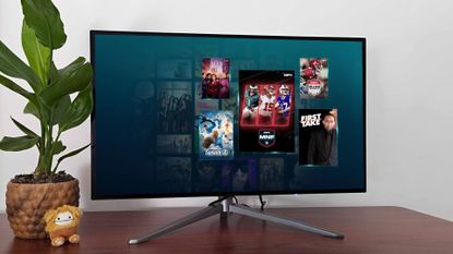 A monitor on a wooden surface with a plant and a plushie, with the screen displaying Disney Plus, Hulu, and ESPN content