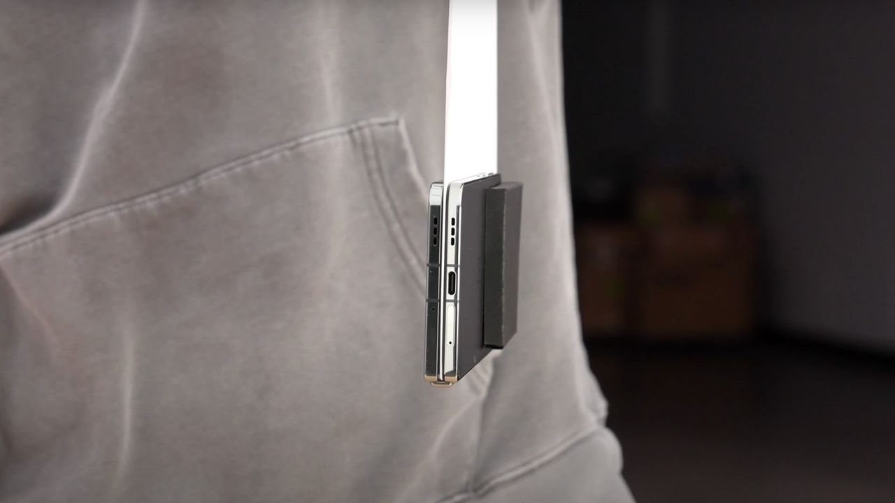The OnePlus Open closed and hanging from a piece of paper