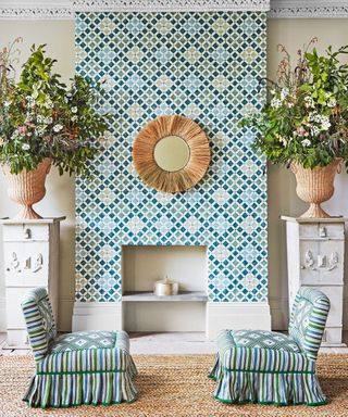 Colorful wallpapered fireplace, two patterned chairs, vases of flowers