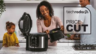 A family cooking with a Ninja cooker in their kitchen next to a sign saying "Price Cut"