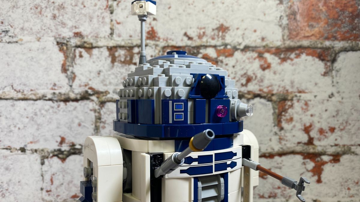 Lego R2-D2 seen against a brick pattern, with tool arms and periscope out