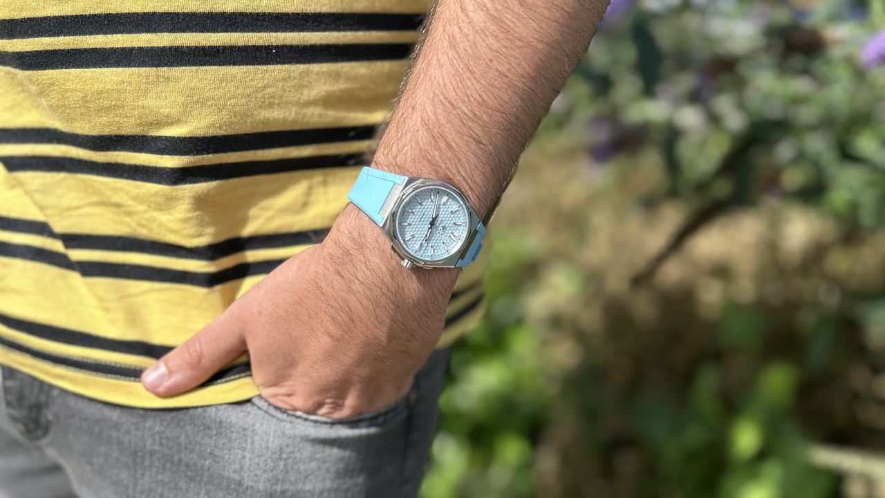 The Christopher Ward The Twelve 36mm in Blue worn on a wrist against a green background