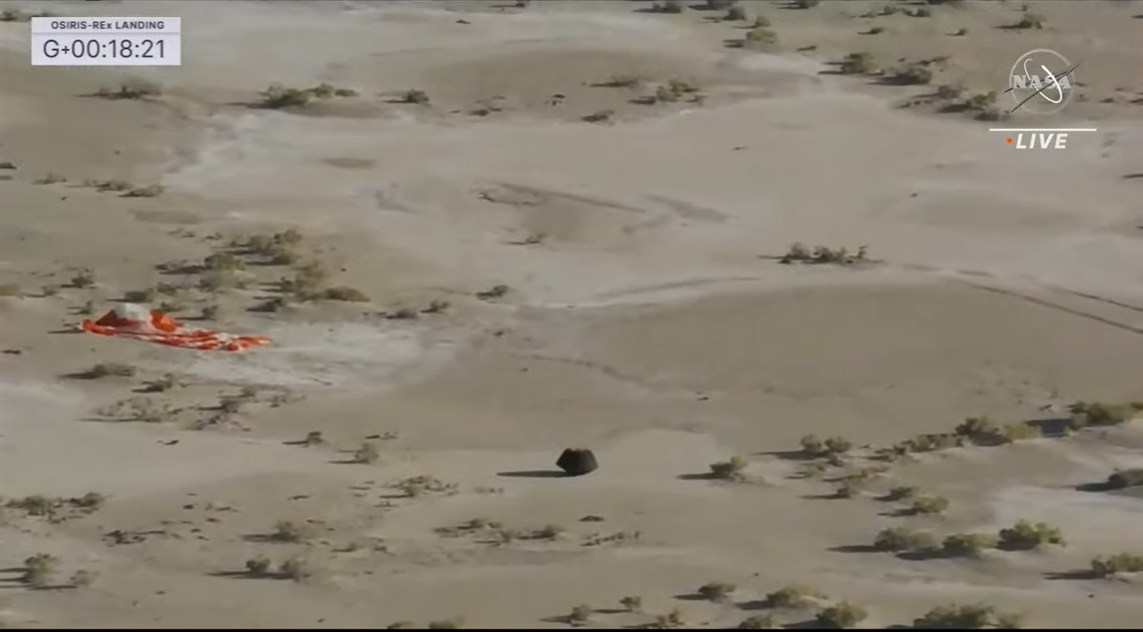 The sample capsule is seen next to the parachute on the ground.