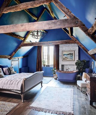 bedroom with vaulted ceiling, blue walls and blue and copper freestanding bath in 12th century Cotswolds country house