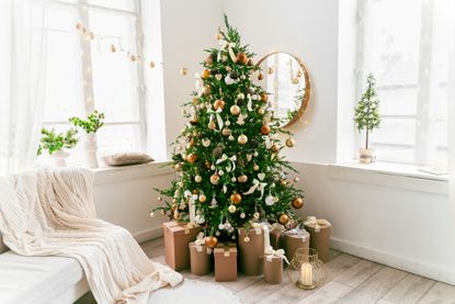 White and spacious domestic living room decorated with Christmas fir tree and pastel holiday decor. Festive craft gift boxes and wrapped presents for family and friends. Cozy celebrations at home