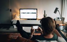 A man lounging on a couch streams from his phone to a television in a living room.