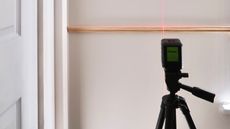 A laser level on tripod being used with red beam shining on wooden dado rail