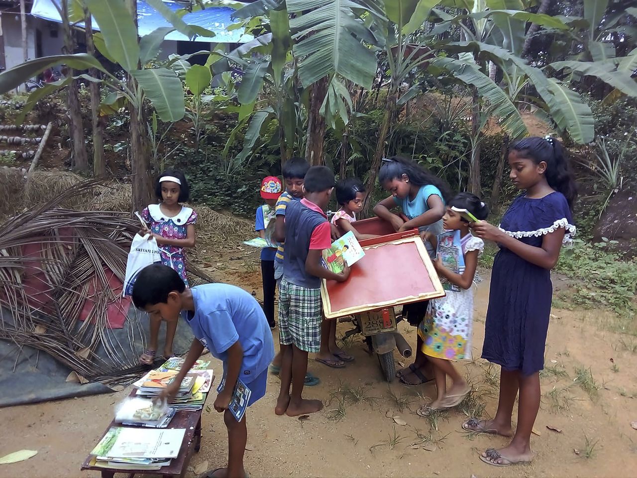 Kids read books brought to them by Mahinda Dasanayaka.