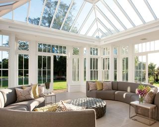Westbury Garden Rooms orangery with curved brown sofas, marble side tables, and floor-to-ceiling doors and windows