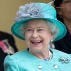 Queen Elizabeth II wears a turquoise green outfit and matching hat while smiling at Kate Middleton, who wears a blue suit