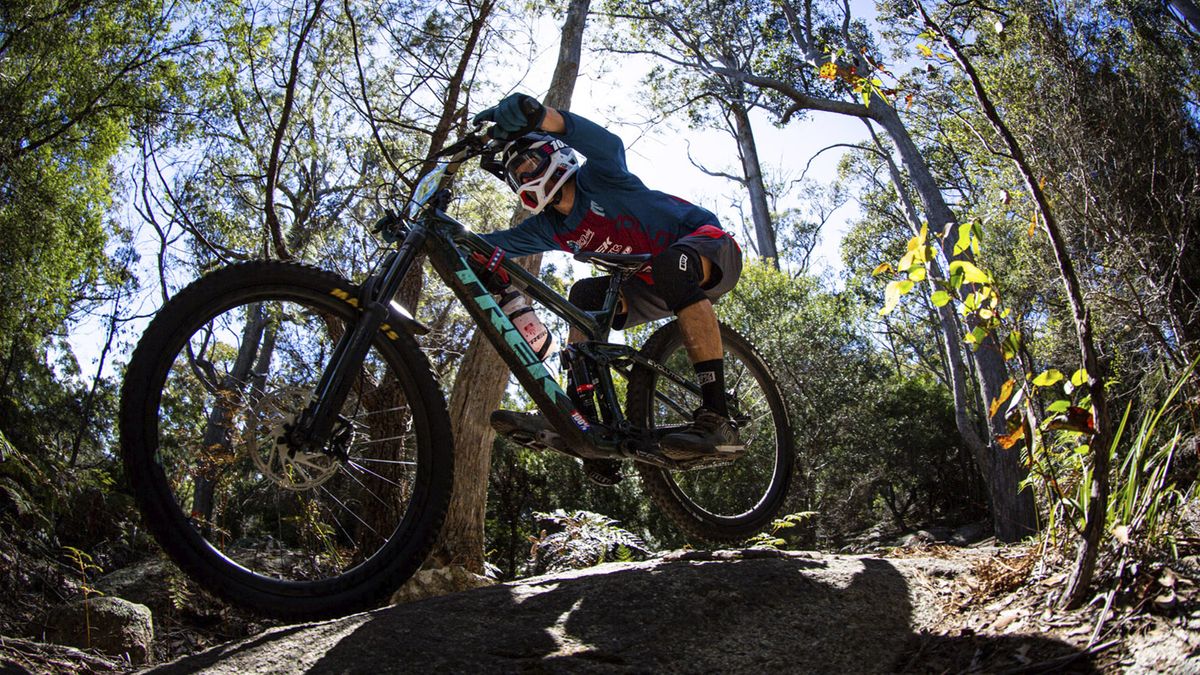 A mountain biker with a full-face helmet soaring down a rocky descent on a Trek bike