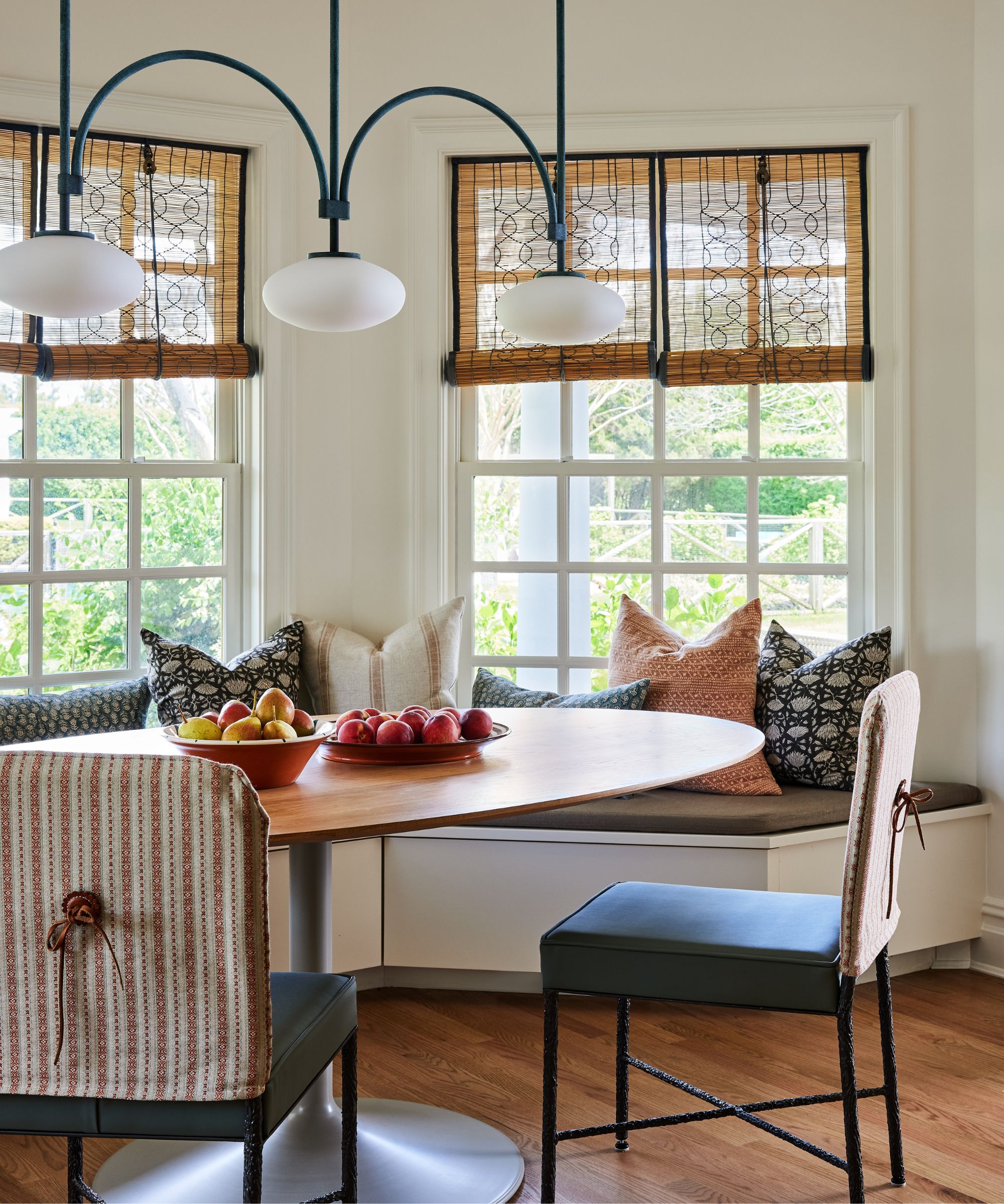 Breakfast nook with iron dining chairs, banquette seating, pendant light, printed cushions and round wood table