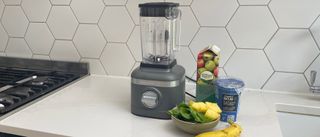 KitchenAid K150 blender on a kitchen countrop with a pile of fruit and vegetables ready to be made into a smoothie
