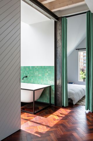 Bathroom with green tiles and walk through to bedroom covered by green curtains