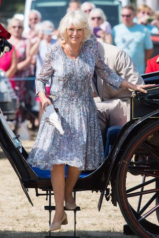 Queen Camilla wearing a floral pleated dress stepping down from a carriage