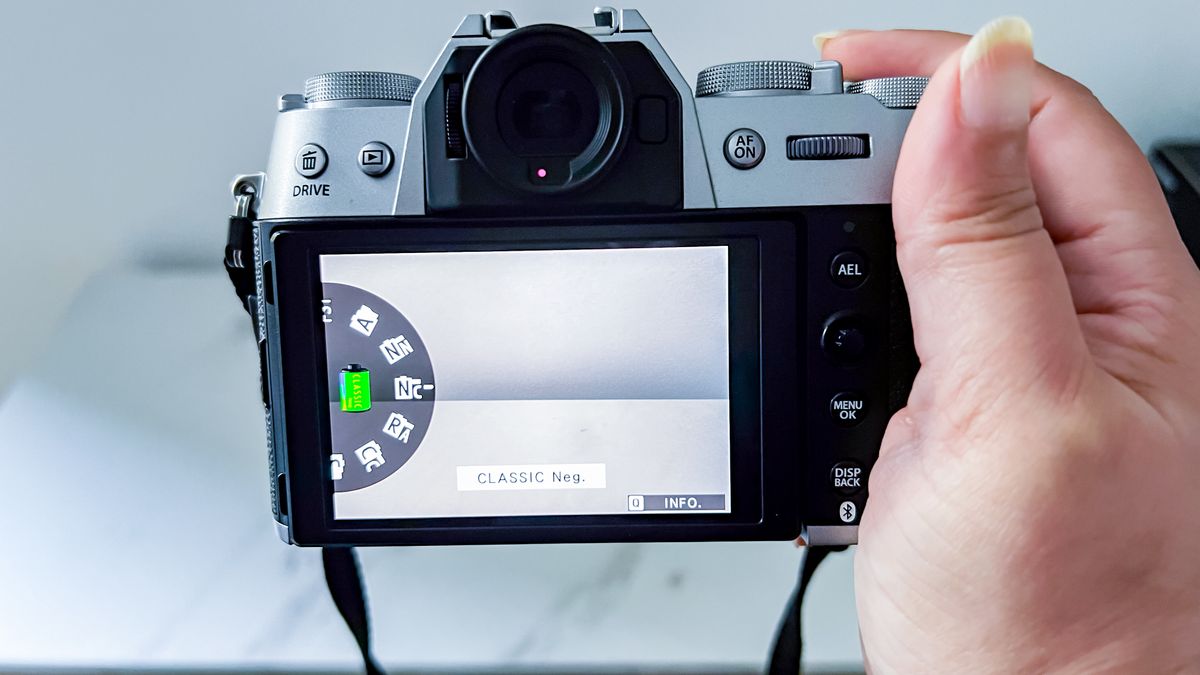 A hand holding the Fujifilm X-T50 with a Film Simulation displayed on the rear monitor