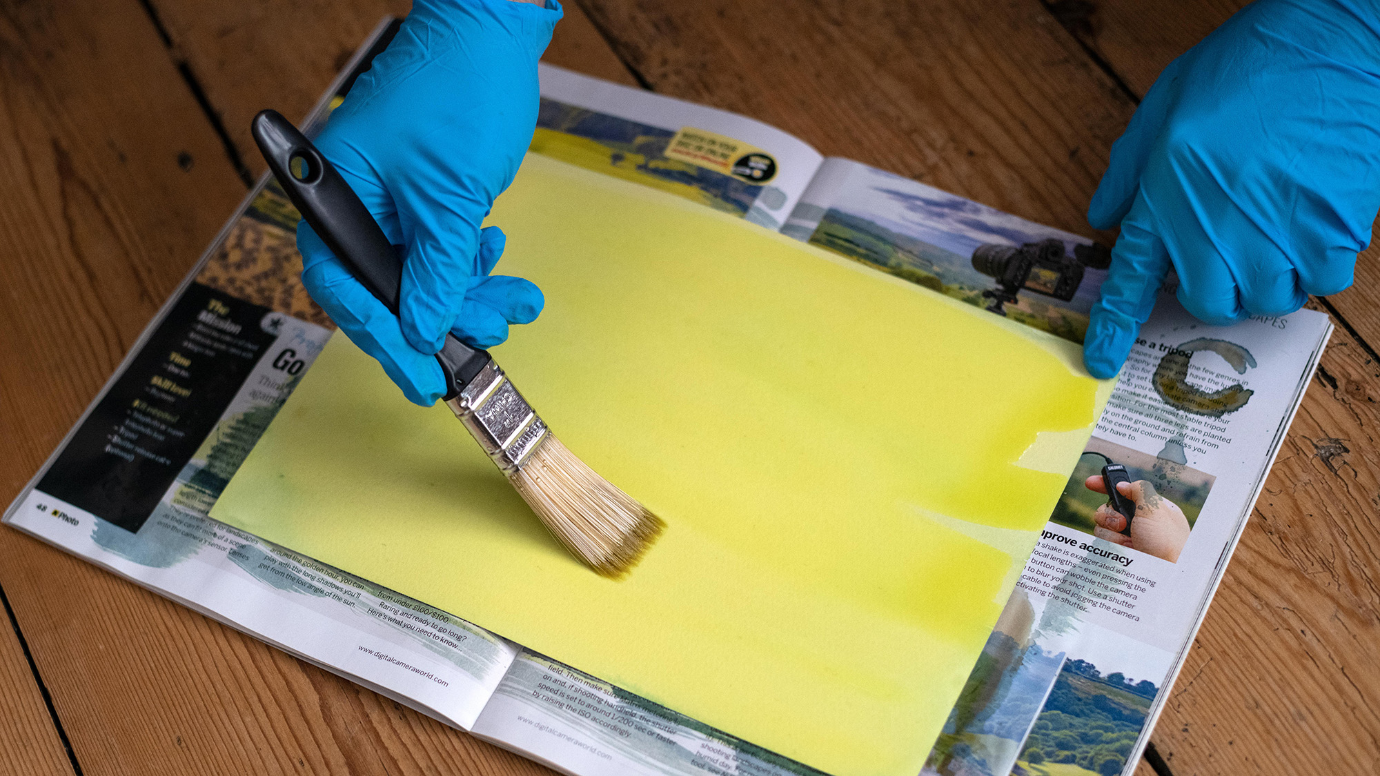 Gloved hands holding a paintbrush and covering paper with yellow sensitizer solution