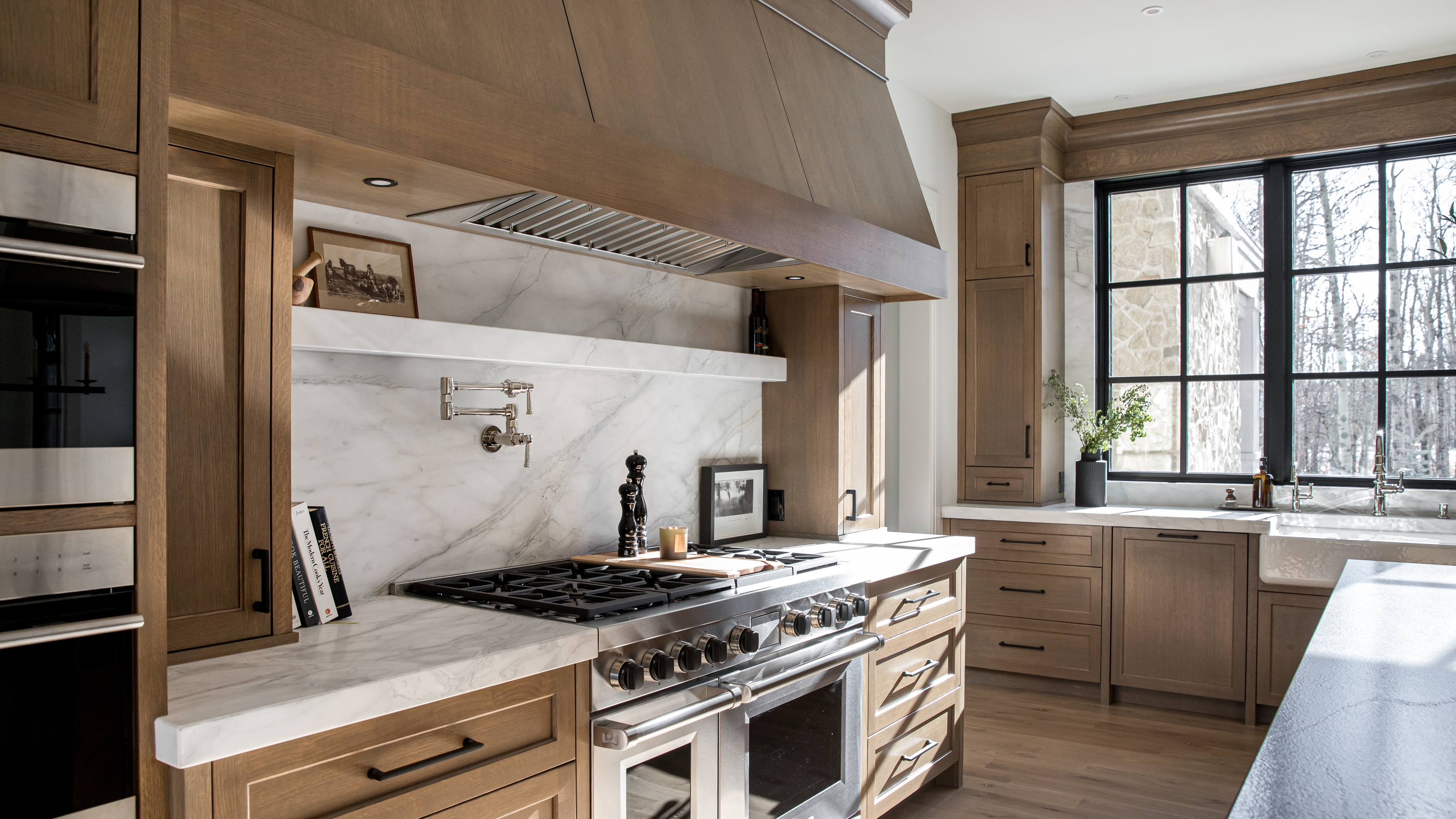 A kitchen with wooden shaker cabinetry and a large range oven in an alcove with a marble countersplash and built-in shelf 