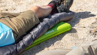 The bottom of an Exped Ultra 3R sleeping mat, with a sleeping bag and legs of a man lying on it.