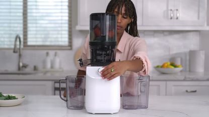 A woman using the Nama C2 as a juicer on a marble countertop