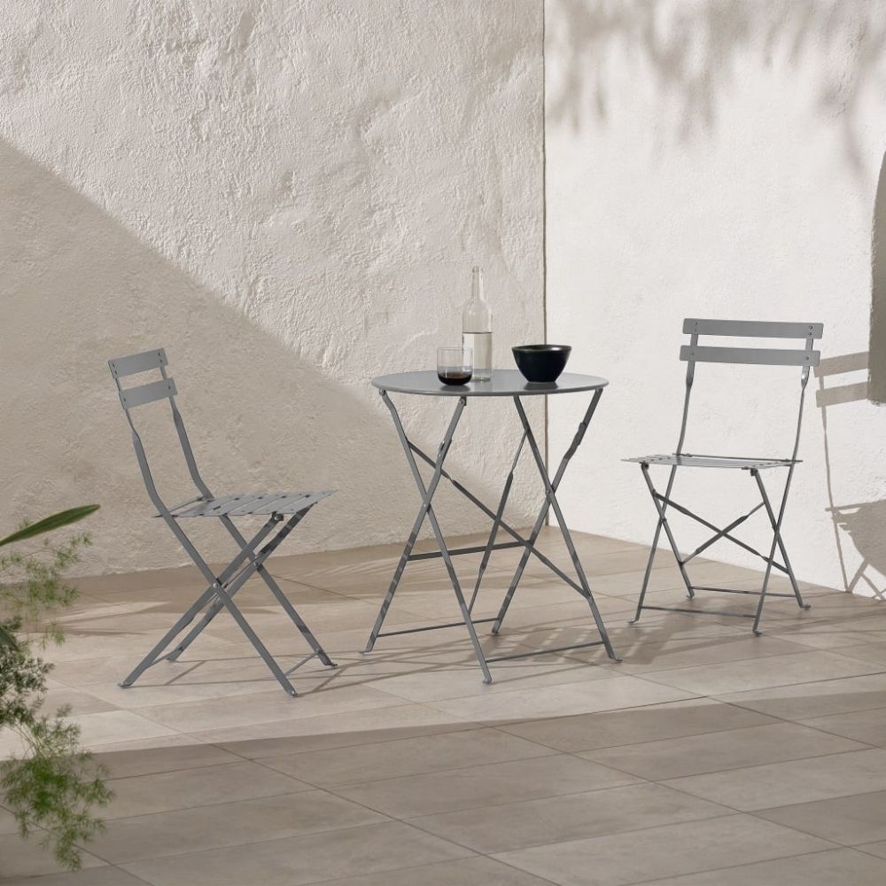 Two metal chairs and round table on top of grey tiles next to painted wall