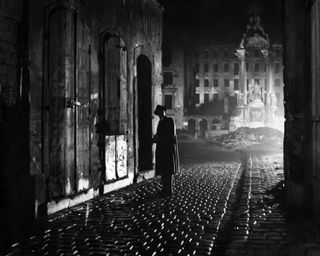 a man standing in an alley down a city street in a black and white still from The Third Man