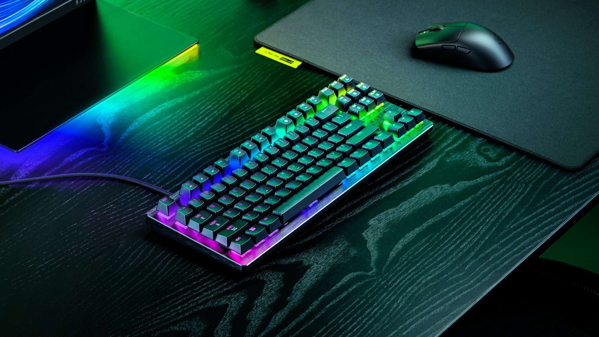 Razer Huntsman V3 HE TKL gaming keyboard on a black desk with accessories