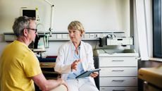 A doctor consults with an older, male patient in a clinical setting.