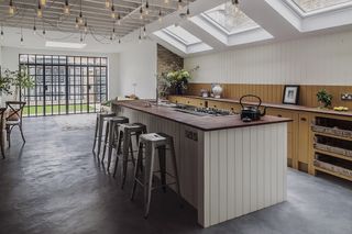 A wood panelled kitchen island with rustic metal bar stools and saloon fairy lights overhead.