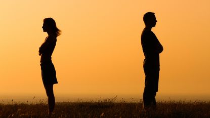 A couple stand facing away from each other with arms crossed