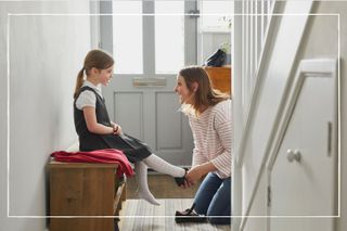 mother helping child put on school shoes in hallway at home