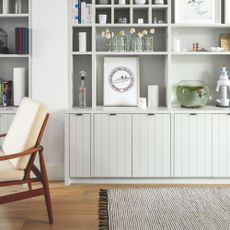 Cream built-in bookcase filled with books, vases, and other accessories, with a rug and an accent chair underneath