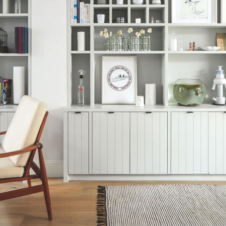 Cream built-in bookcase filled with books, vases, and other accessories, with a rug and an accent chair underneath