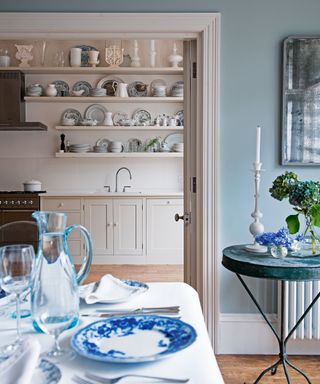 An example of kitchen storage ideas showing a blue and cream kitchen with a dining table and open shelving above a sink in the background