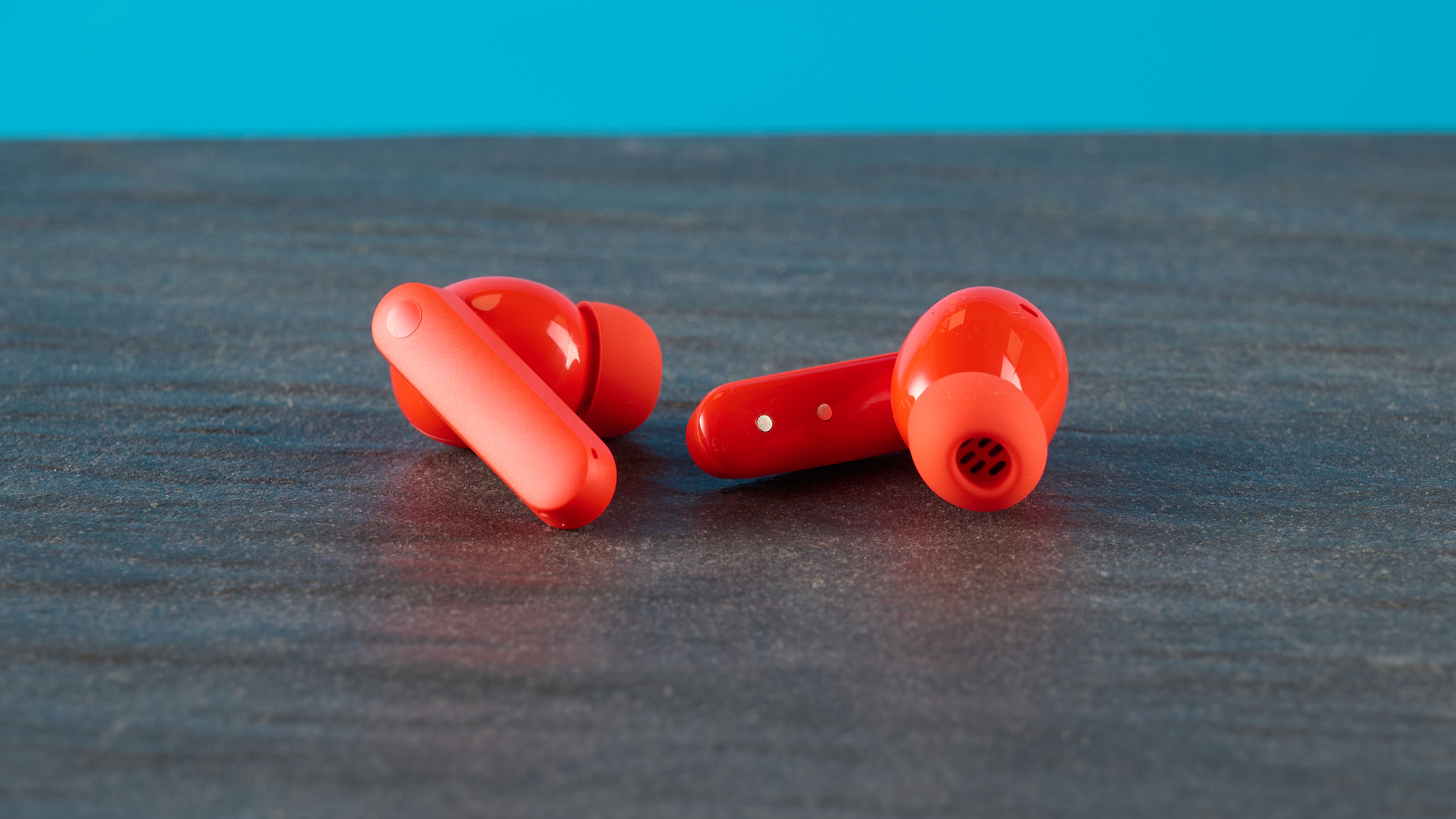 cmf buds 2a in the orange colorway photographed in front of a blue background