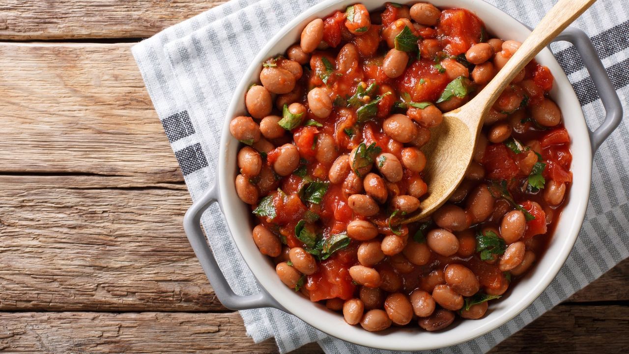 Bean and root vegetable casserole in dish with a wooden spoon