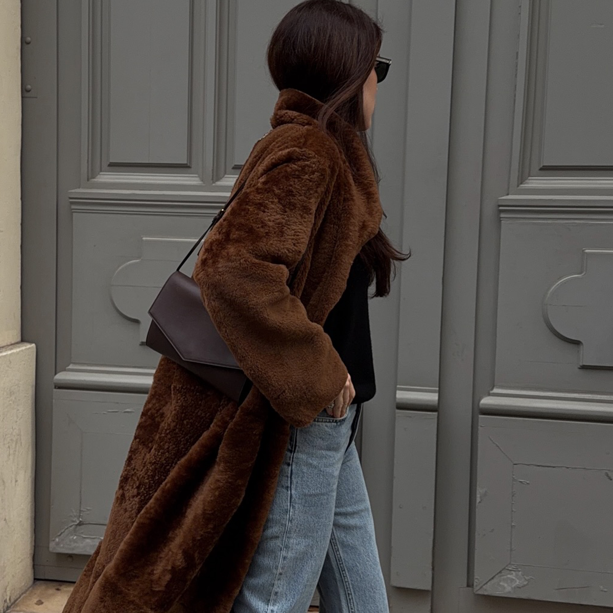 Woman wearing brown fur coat, straight leg denim, and brown bag while walking on the streets of Paris, France