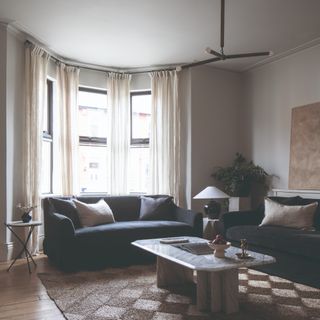 A modern living room with a pendant ceiling light, two dark sofas and a table lamp on a side table